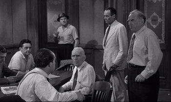 Movie still from “12 Angry Men” (1957), directed by Sidney Lumet – A black and white photo of a group of people; Medium shot, Over the shoulder angle