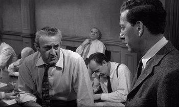 Movie still from “12 Angry Men” (1957), directed by Sidney Lumet – A black and white photo of a group of men in a room; Medium shot, Over the shoulder angle