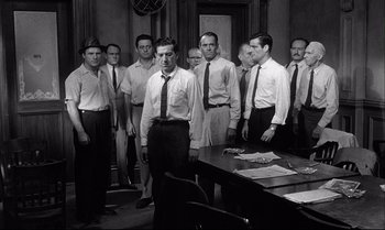 Movie still from “12 Angry Men” (1957), directed by Sidney Lumet – A black and white photo of a group of men standing around a table; Medium shot, High angle