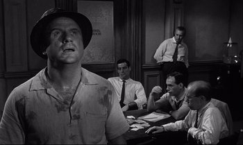 Movie still from “12 Angry Men” (1957), directed by Sidney Lumet – A black - and - white photo of a man in front of a group of men; Medium shot, Low angle