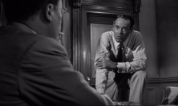 Movie still from “12 Angry Men” (1957), directed by Sidney Lumet – A man sitting on the ground in front of another man; Medium shot, Over the shoulder angle