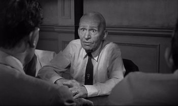 Movie still from “12 Angry Men” (1957), directed by Sidney Lumet – An older man sitting at a table in front of two other people; Medium shot, Over the shoulder angle