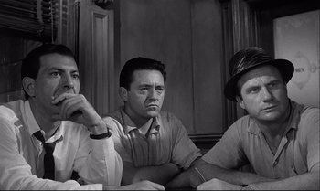 Movie still from “12 Angry Men” (1957), directed by Sidney Lumet – A group of men sitting next to each other in front of a wall; Medium shot, Low angle