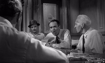 Movie still from “12 Angry Men” (1957), directed by Sidney Lumet – A group of men sitting at a table talking to each other; Medium shot, Over the shoulder angle