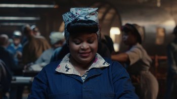 Movie still from “A League of Their Own” (2022), created by Abbi Jacobson – A woman with a head scarf is smiling for the camera; Close Up shot, Over the shoulder angle