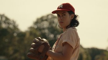Movie still from “A League of Their Own” (2022), created by Abbi Jacobson – A woman in a baseball uniform holding a baseball glove; Close Up shot, Low angle
