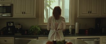 Movie still from “Hateship Loveship” (2013), directed by Liza Johnson – A woman standing in front of a window in a kitchen; Medium shot, Low angle