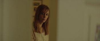 Movie still from “Hateship Loveship” (2013), directed by Liza Johnson – A young woman looking at the camera in a room; Close Up shot, Over the shoulder angle