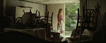 Movie still from “Hateship Loveship” (2013), directed by Liza Johnson – A woman standing in front of a window looking outside; Wide shot, Over the shoulder angle