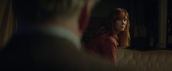 Movie still from “Hateship Loveship” (2013), directed by Liza Johnson – A woman in a red shirt is sitting in a dark room; Medium shot, Over the shoulder angle