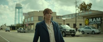 Movie still from “Hateship Loveship” (2013), directed by Liza Johnson – A woman standing in a parking lot wearing a blue jacket; Medium shot, Low angle