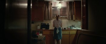 Movie still from “Hateship Loveship” (2013), directed by Liza Johnson – A woman standing in a kitchen looking in the mirror; Wide shot, High angle