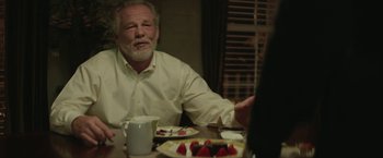Movie still from “Hateship Loveship” (2013), directed by Liza Johnson – An older man sitting at a table in front of a plate of cake; Medium shot, Over the shoulder angle