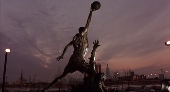Movie still from “He Got Game” (1998), directed by Spike Lee – A statue of a man playing basketball in a park; Wide shot, Low angle