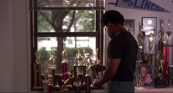Movie still from “He Got Game” (1998), directed by Spike Lee – A man standing in front of a table filled with trophies; Medium shot, Low angle