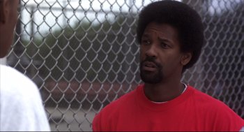 Movie still from “He Got Game” (1998), directed by Spike Lee – A man in a red t - shirt is standing in front of a chain link fence; Close Up shot, Over the shoulder angle