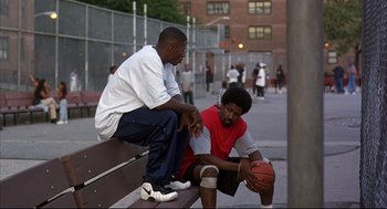 Movie still from “He Got Game” (1998), directed by Spike Lee – Two men sitting on a bench with a basketball in front of them; Medium shot, Over the shoulder angle