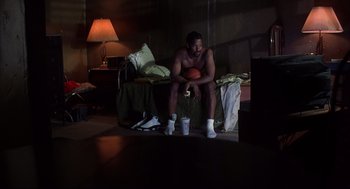 Movie still from “He Got Game” (1998), directed by Spike Lee – A man sitting on a bed holding a basketball; Wide shot, High angle