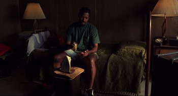 Movie still from “He Got Game” (1998), directed by Spike Lee – A man sitting on a couch holding a cell phone; Medium shot, Low angle