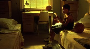 Movie still from “He Got Game” (1998), directed by Spike Lee – A young man sitting on a bed in front of a desk; Medium shot, Low angle