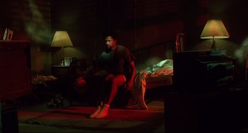 Movie still from “He Got Game” (1998), directed by Spike Lee – A man sitting on the ground in a dark room; Wide shot, Low angle