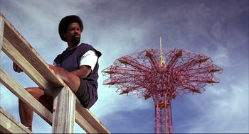 Movie still from “He Got Game” (1998), directed by Spike Lee – A man sitting on top of a wooden railing next to a ferris wheel; Wide shot, Low angle