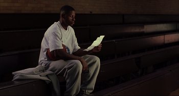 Movie still from “He Got Game” (1998), directed by Spike Lee – A man sitting on a bench looking at a piece of paper; Medium shot, Low angle