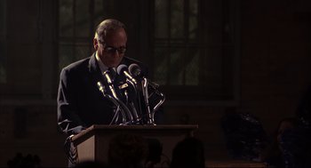 Movie still from “He Got Game” (1998), directed by Spike Lee – A man standing at a podium with microphones in front of him; Medium shot, Over the shoulder angle