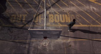 Movie still from “He Got Game” (1998), directed by Spike Lee – A person standing in a parking lot next to a basketball hoop; Extreme Wide shot, Overhead angle