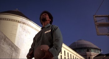Movie still from “He Got Game” (1998), directed by Spike Lee – A man standing in front of a building holding a frisbee; Medium shot, Low angle
