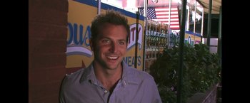 Movie still from “He's Just Not That Into You” (2009), directed by Ken Kwapis – A man smiling for the camera in front of an american flag; Close Up shot, Over the shoulder angle