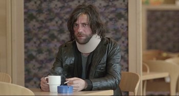 Movie still from “Head-On” (2004), directed by Fatih Akin – A man wearing a neck brace sitting at a table with a cup of coffee; Medium shot, Low angle
