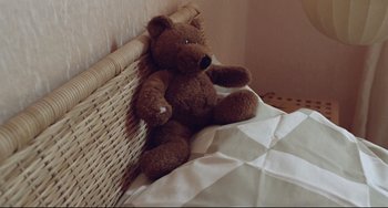 Movie still from “Head-On” (2004), directed by Fatih Akin – A brown teddy bear sitting on top of a bed next to a white blanket; Close Up shot, High angle