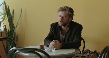 Movie still from “Head-On” (2004), directed by Fatih Akin – A man sitting at a table with a drink in front of him; Medium shot, Over the shoulder angle