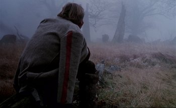 Movie still from “Heart of Glass” (1976), directed by Werner Herzog – A man sitting on the ground in a field; Wide shot, Over the shoulder angle