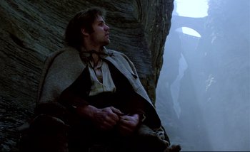 Movie still from “Heart of Glass” (1976), directed by Werner Herzog – A man sitting on top of a cliff looking up at the sky; Medium shot, Low angle