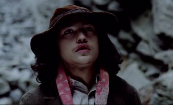 Movie still from “Heart of Glass” (1976), directed by Werner Herzog – A man wearing a brown hat and a pink neck scarf; Close Up shot, Low angle