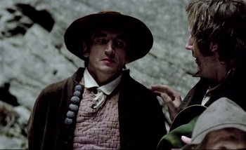 Movie still from “Heart of Glass” (1976), directed by Werner Herzog – A man wearing a hat and a jacket talking to another man; Close Up shot, Over the shoulder angle