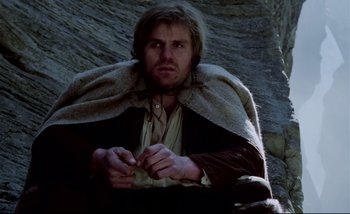 Movie still from “Heart of Glass” (1976), directed by Werner Herzog – A man sitting on the ground wearing a cape; Medium shot, Low angle