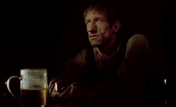 Movie still from “Heart of Glass” (1976), directed by Werner Herzog – A man sitting in front of a lit candle in a dark room; Close Up shot, Low angle