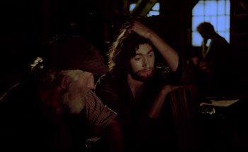 Movie still from “Heart of Glass” (1976), directed by Werner Herzog – A man with long hair is sitting next to another man; Close Up shot, Over the shoulder angle