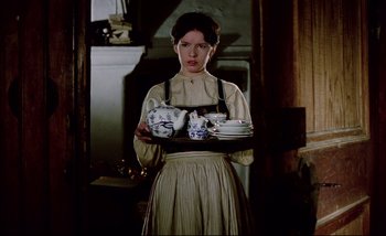 Movie still from “Heart of Glass” (1976), directed by Werner Herzog – A woman holding a tray of dishes in a kitchen; Medium shot, Low angle