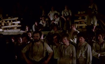 Movie still from “Heart of Glass” (1976), directed by Werner Herzog – A group of people sitting and standing in the dark; Wide shot, High angle