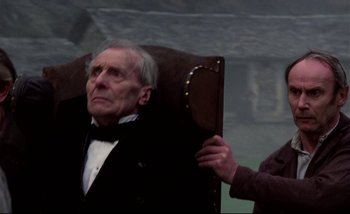 Movie still from “Heart of Glass” (1976), directed by Werner Herzog – An older man sitting in a chair with a woman; Medium shot, High angle