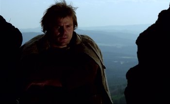 Movie still from “Heart of Glass” (1976), directed by Werner Herzog – A man standing on top of a hill with a mountain in the background; Close Up shot, Low angle