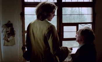 Movie still from “Heart of Glass” (1976), directed by Werner Herzog – A man standing next to another man in front of a window; Medium shot, Over the shoulder angle