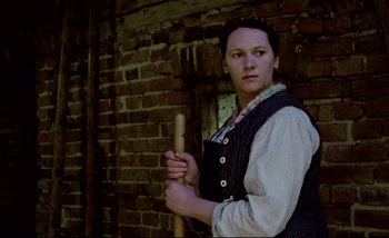 Movie still from “Heart of Glass” (1976), directed by Werner Herzog – A woman holding a wooden stick in front of a brick wall; Medium shot, Low angle