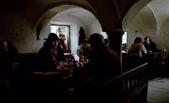 Movie still from “Heart of Glass” (1976), directed by Werner Herzog – A group of people sitting at a table drinking beer; Wide shot, Over the shoulder angle