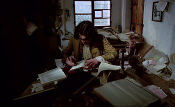 Movie still from “Heart of Glass” (1976), directed by Werner Herzog – A man sitting at a desk writing on a piece of paper; Medium shot, High angle