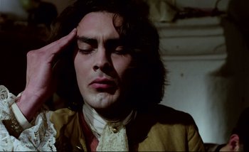 Movie still from “Heart of Glass” (1976), directed by Werner Herzog – A man with long brown hair is holding his hand up to his forehead; Close Up shot, High angle